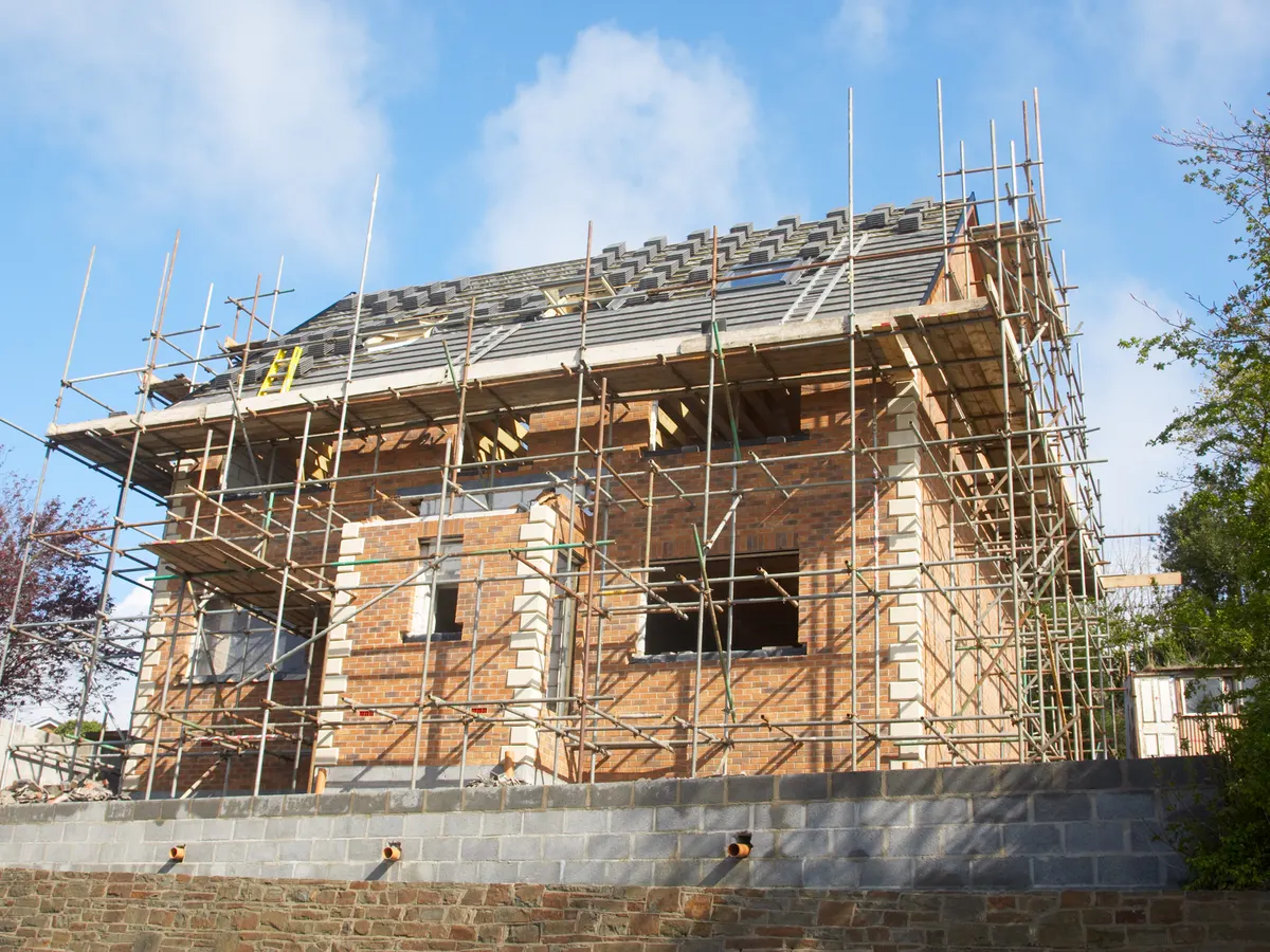 A new house with its roof being tiled inside a full scaffold