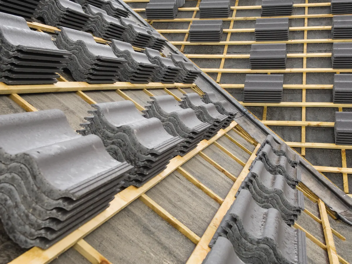 Grey roof tiles being laid over new battens