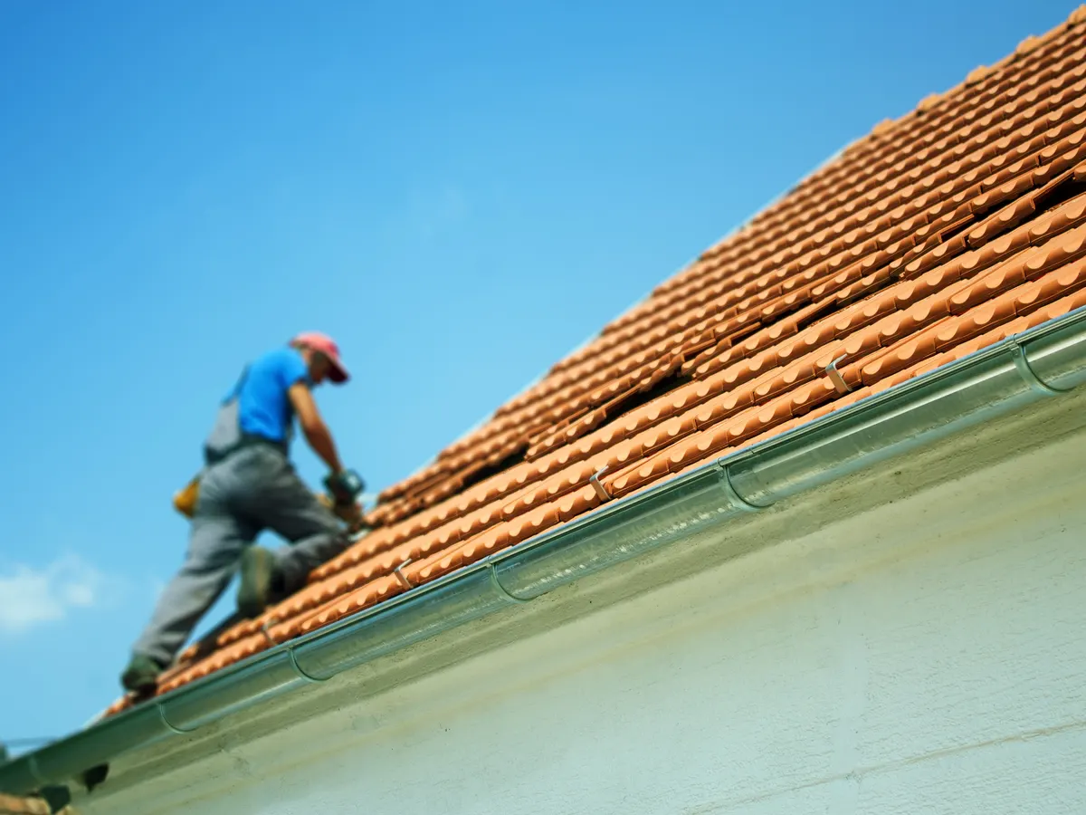 A roofer working along the edge of a clay tiled roof