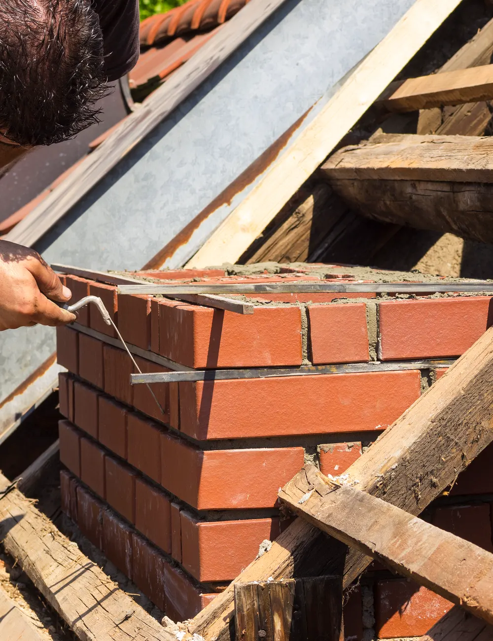 A bricklayer rebuilding a chimney stack on a roof