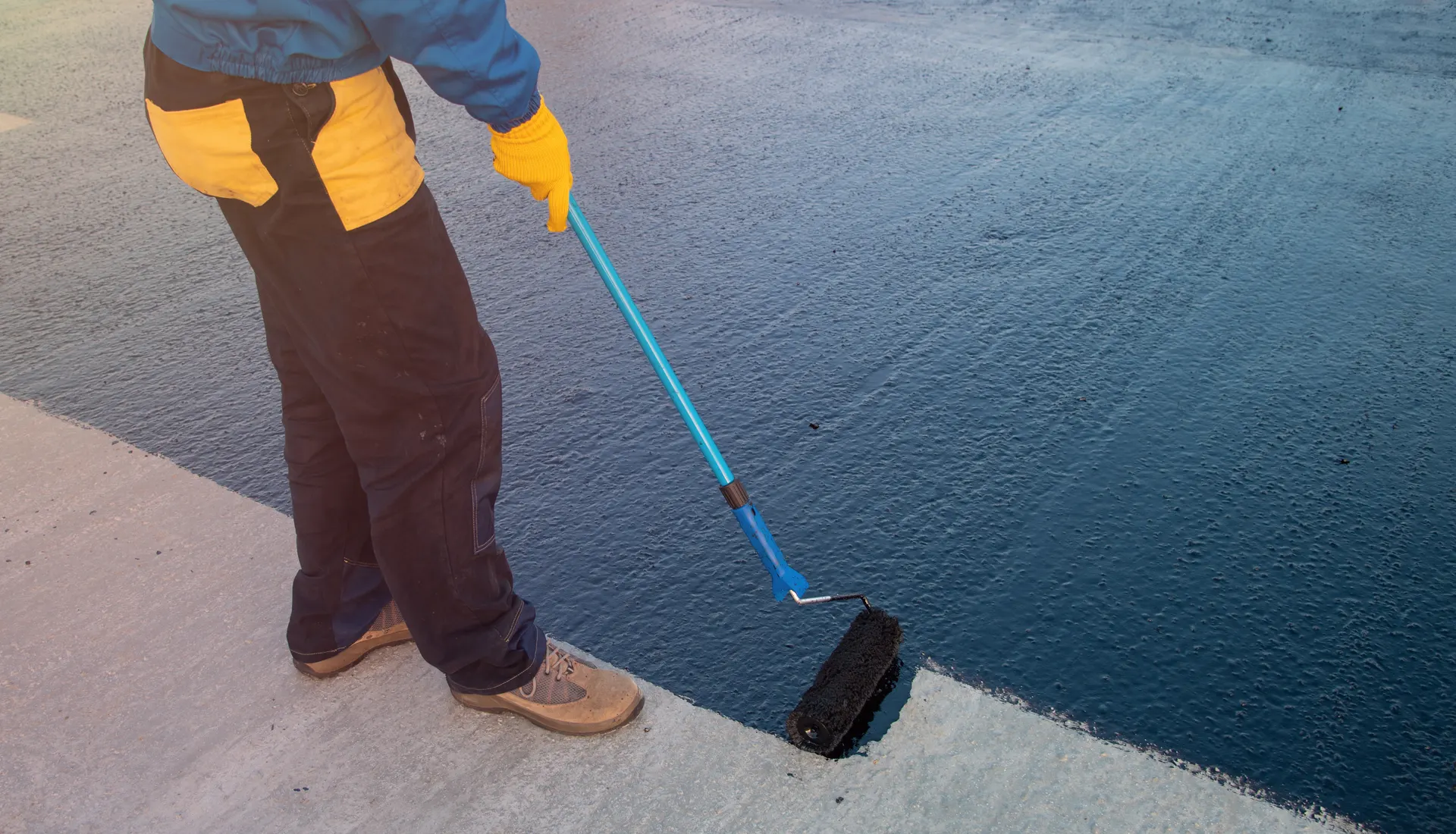 A roofer rolling topcoat onto a fibreglass flat roof