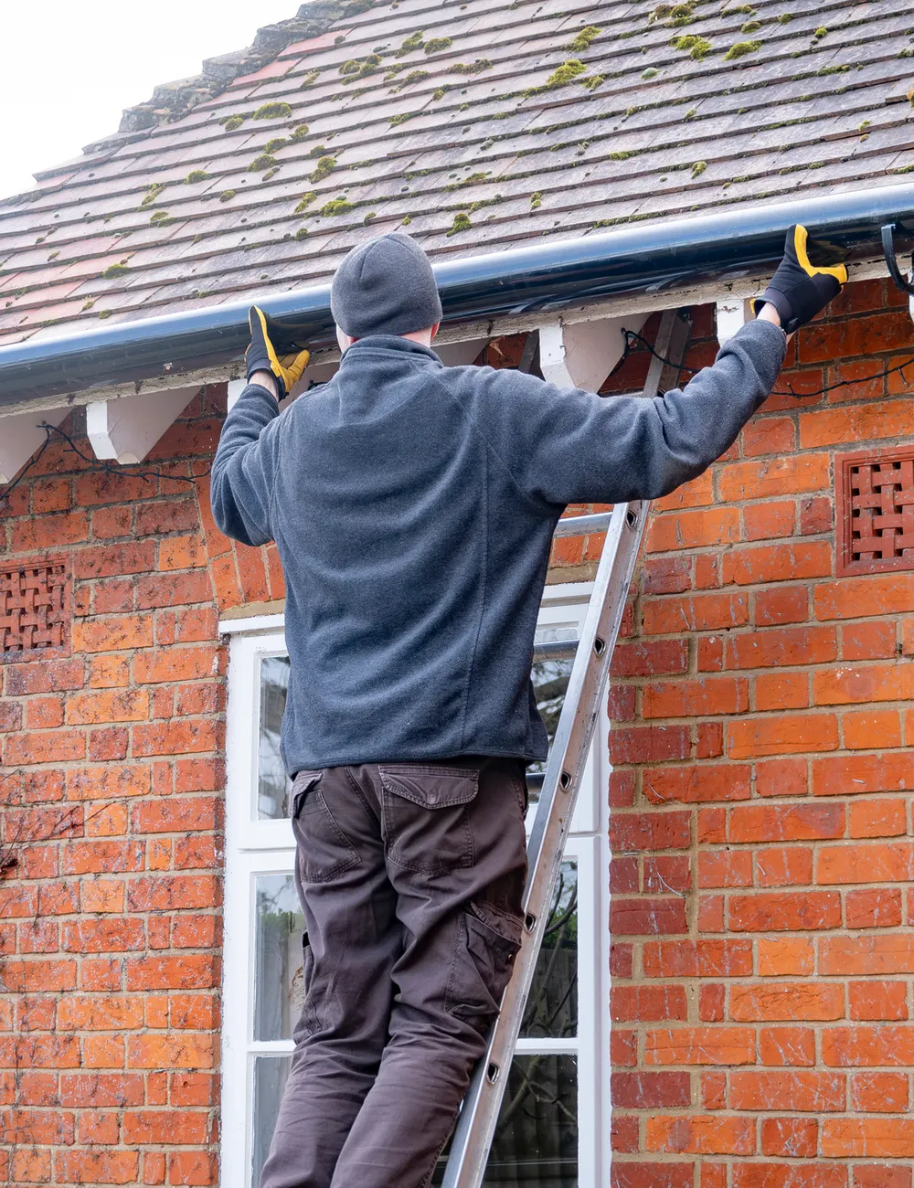 A fitter on a ladder working on a house’s guttering