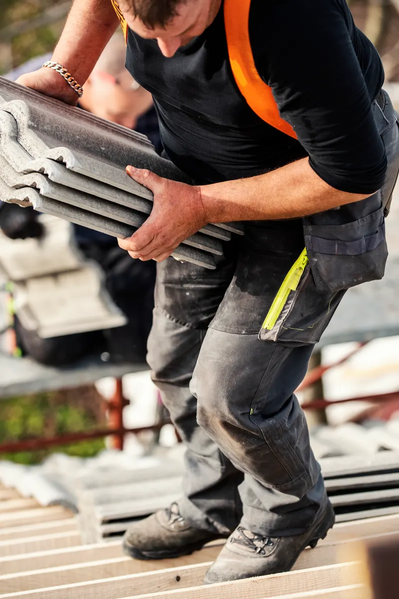 A roofer carrying a stack of new roof tiles