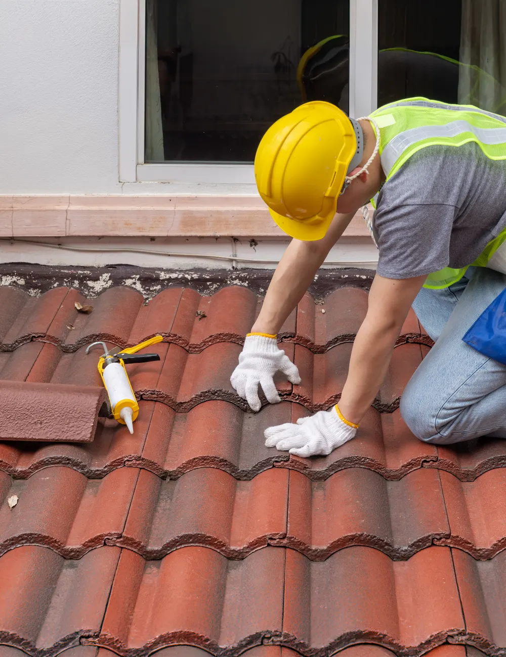 A roofer in a hard hat repairing a clay tiled roof