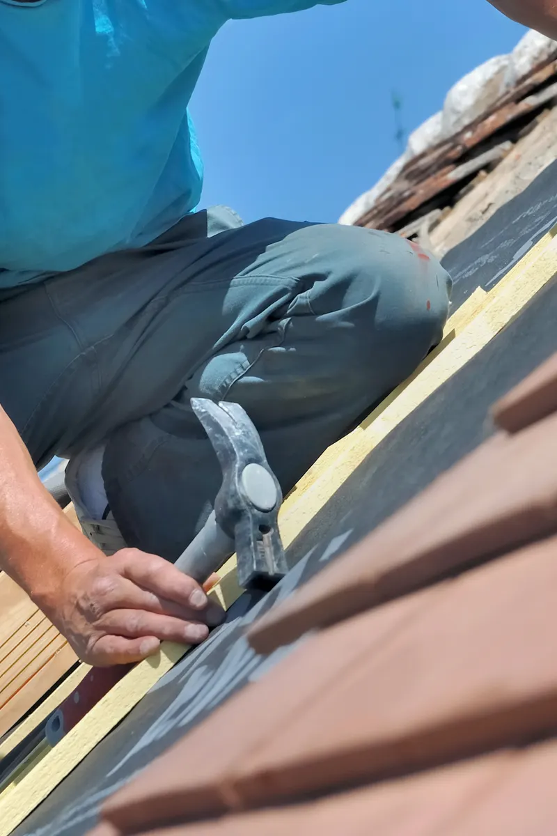 A roofer fixing a roof tile with a hammer
