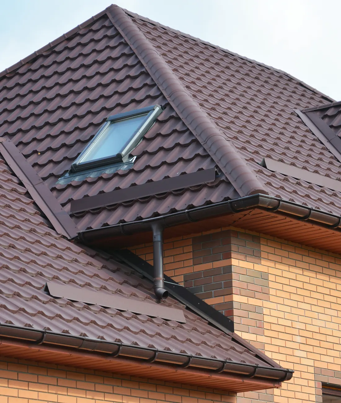 A brown tiled roof with a roof window on a brick house